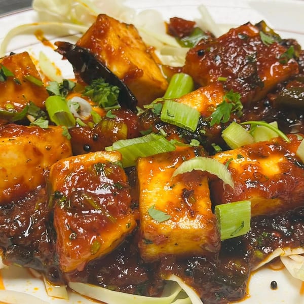 Indian paneer dish with rich red sauce, garnished with green onions and cilantro.