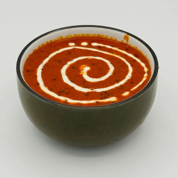 A dark green bowl of red Indian dal, garnished with a white cream swirl.