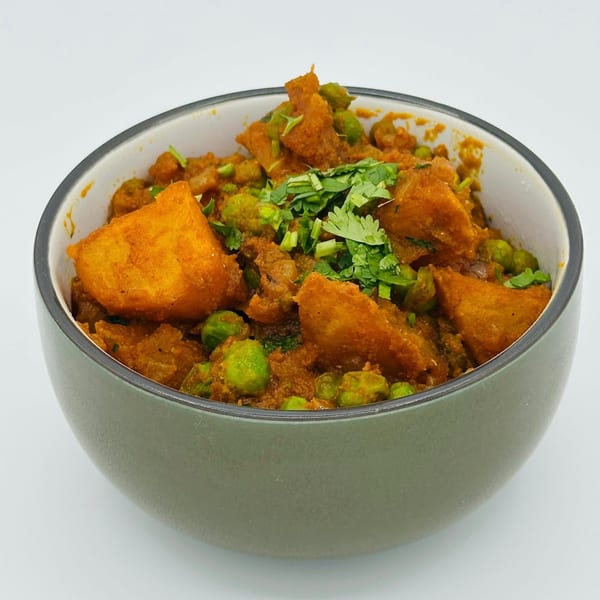 A bowl of Indian Aloo Matar, featuring potatoes and peas in a rich, orange-red curry sauce, garnished with fresh cilantro.