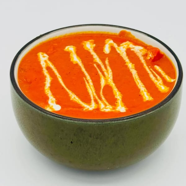 Nawab Indian Restaurant's vibrant orange curry, drizzled with white cream, in a dark green bowl.